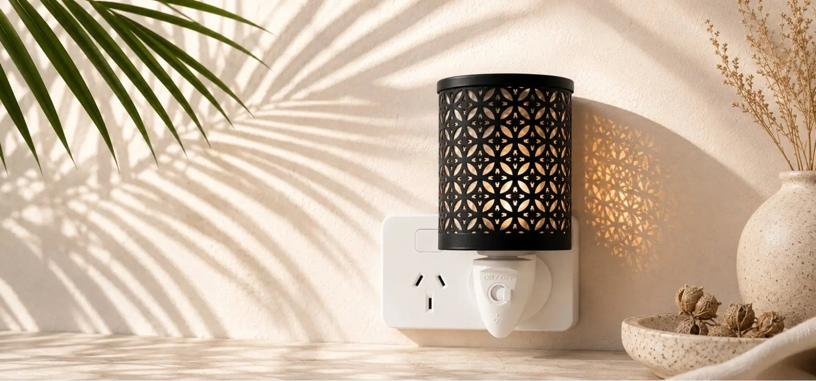 Black cylindrical wax warmer with intricate geometric cutout pattern, plugged into a white wall outlet.