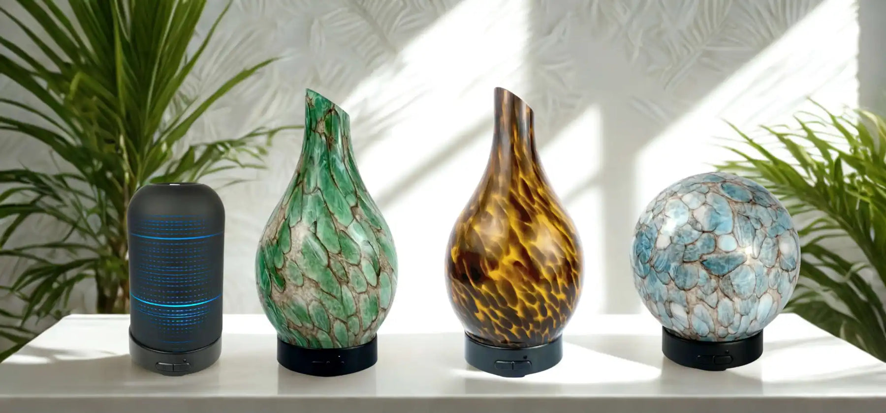 A collection of four decorative diffusers, including a cylindrical speaker-like one and three artistic, textured glass-like designs, one green, one amber, and one blue sphere.