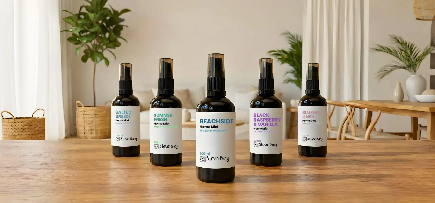 Five dark glass spray bottles with white labels and black caps, each featuring a distinct scent name in colorful text.