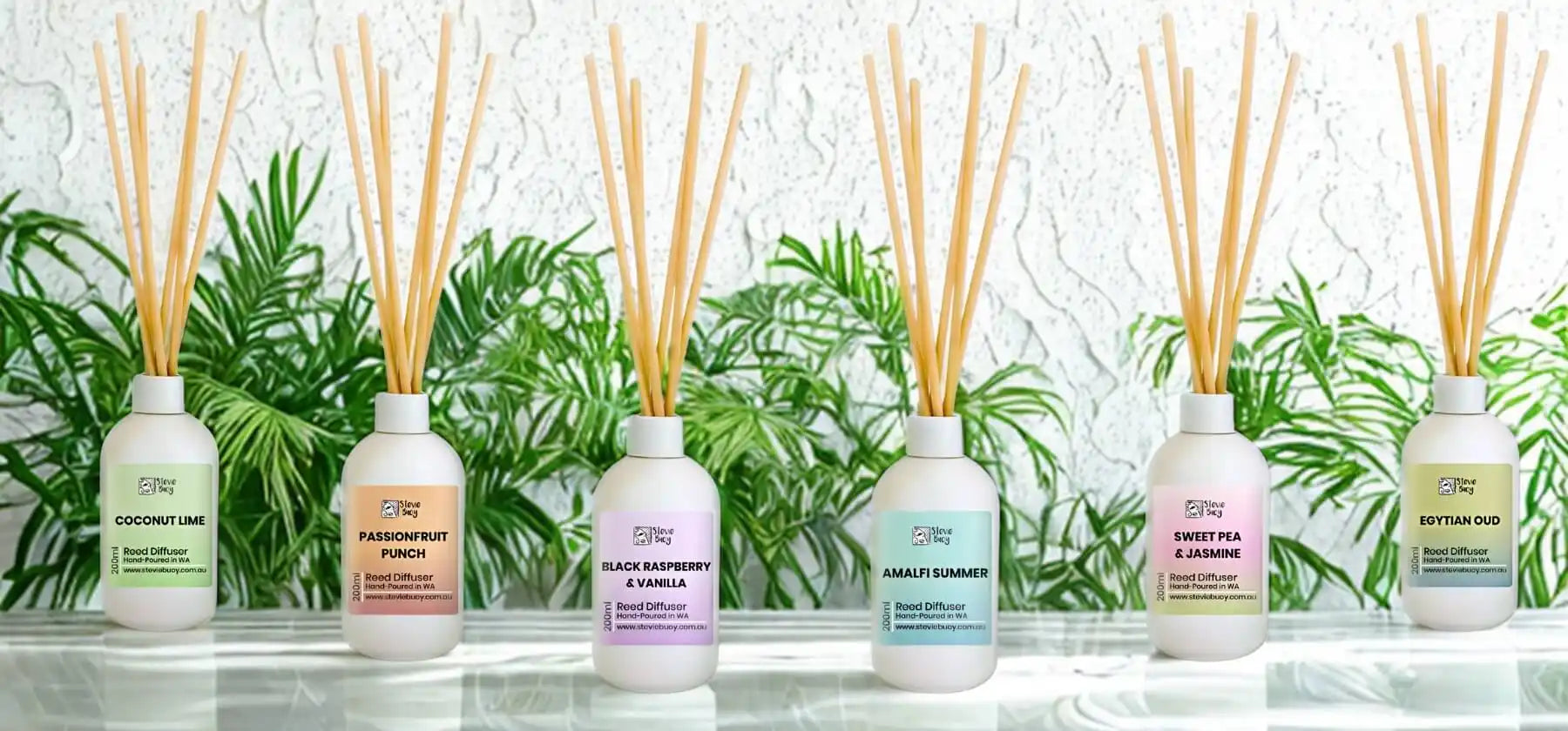 A row of six white reed diffusers with various colored labels and natural reeds.