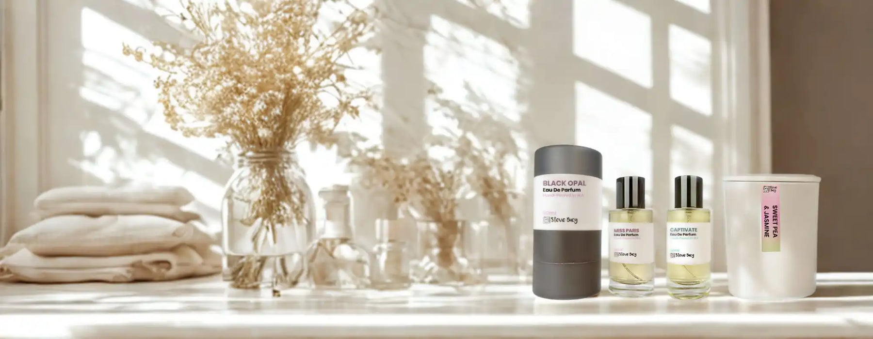A collection of fragrance products, including a cylindrical container, two glass spray bottles, and a lidded candle in a white jar.