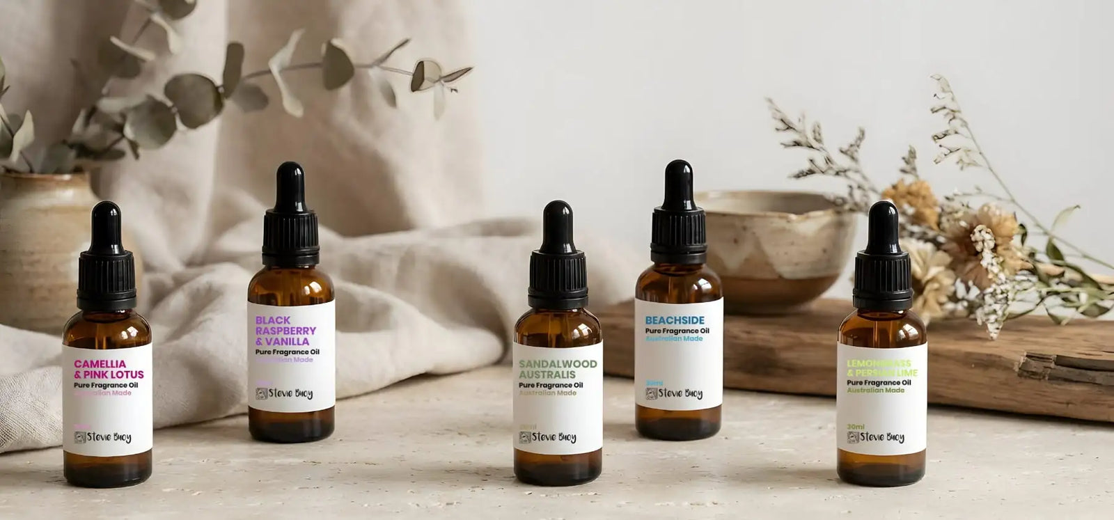 Five amber glass bottles with black dropper caps and white labels, each displaying a different fragrance scent.