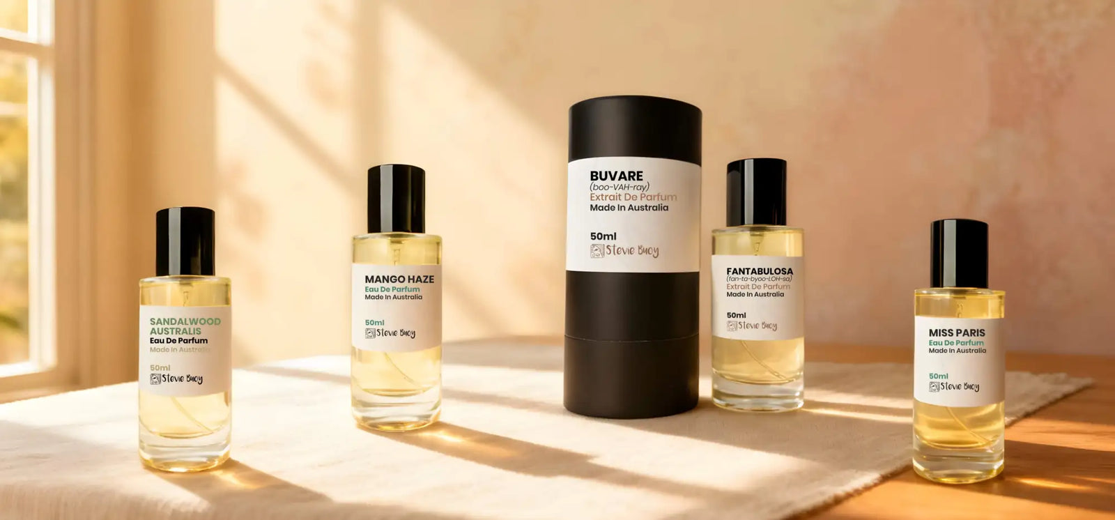 Four glass perfume bottles with black caps and minimalist white labels, alongside a taller cylindrical black container also labeled ’buvare,’ all displaying the brand name “steve seg” on their packaging.