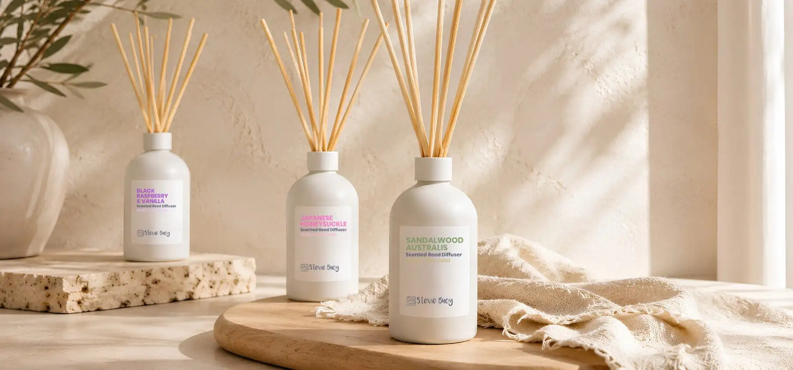 Three white ceramic reed diffusers with wooden sticks, labeled ’sandalwood australia’ and other scents.