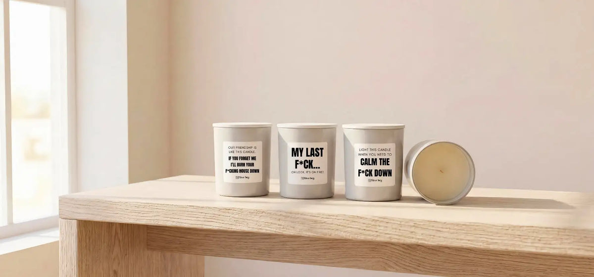 Three white cylindrical candles with black text labels sit on a wooden surface, one lying on its side.