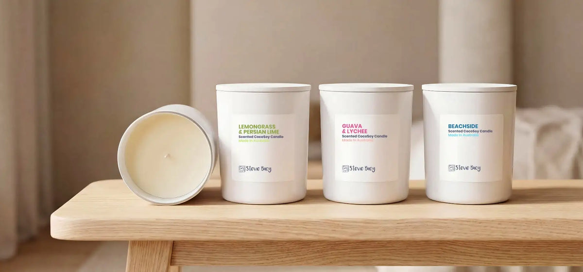 Three white cylindrical scented candle containers with minimalist labels, one tipped over to reveal its creamy wax interior.